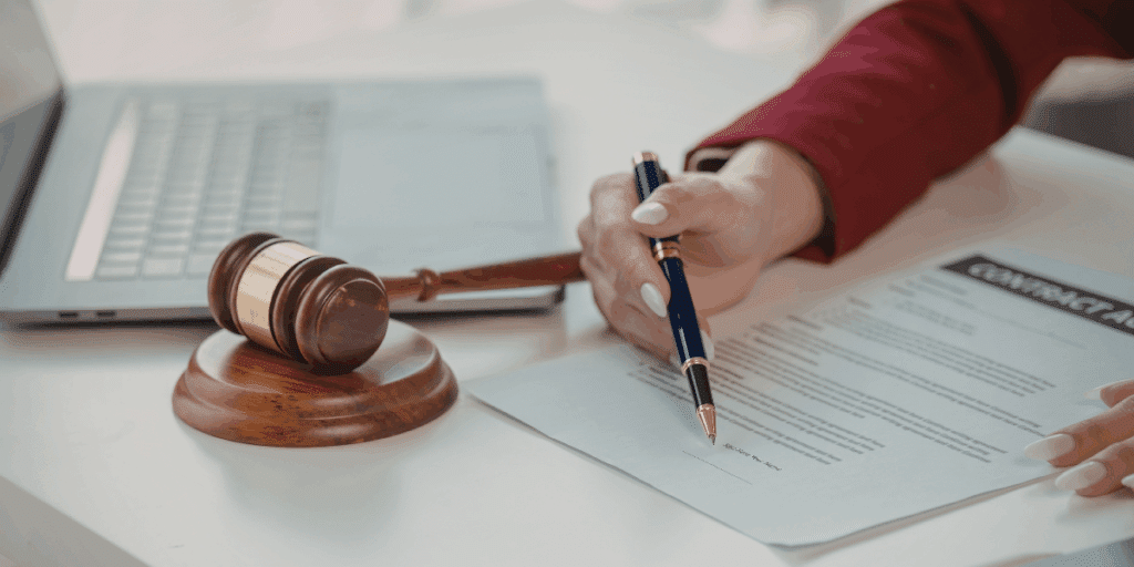 Close-up of a person signing a legal contract next to a wooden gavel and laptop, illustrating the 2026 legal checklist for family and business protection.