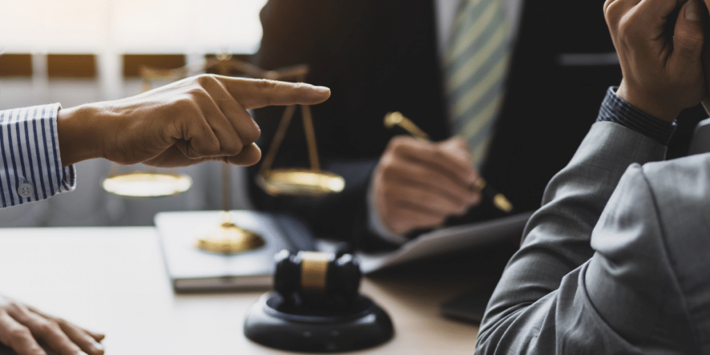 Two business owners in a contract dispute meet with a lawyer, with a gavel and scales of justice on the table