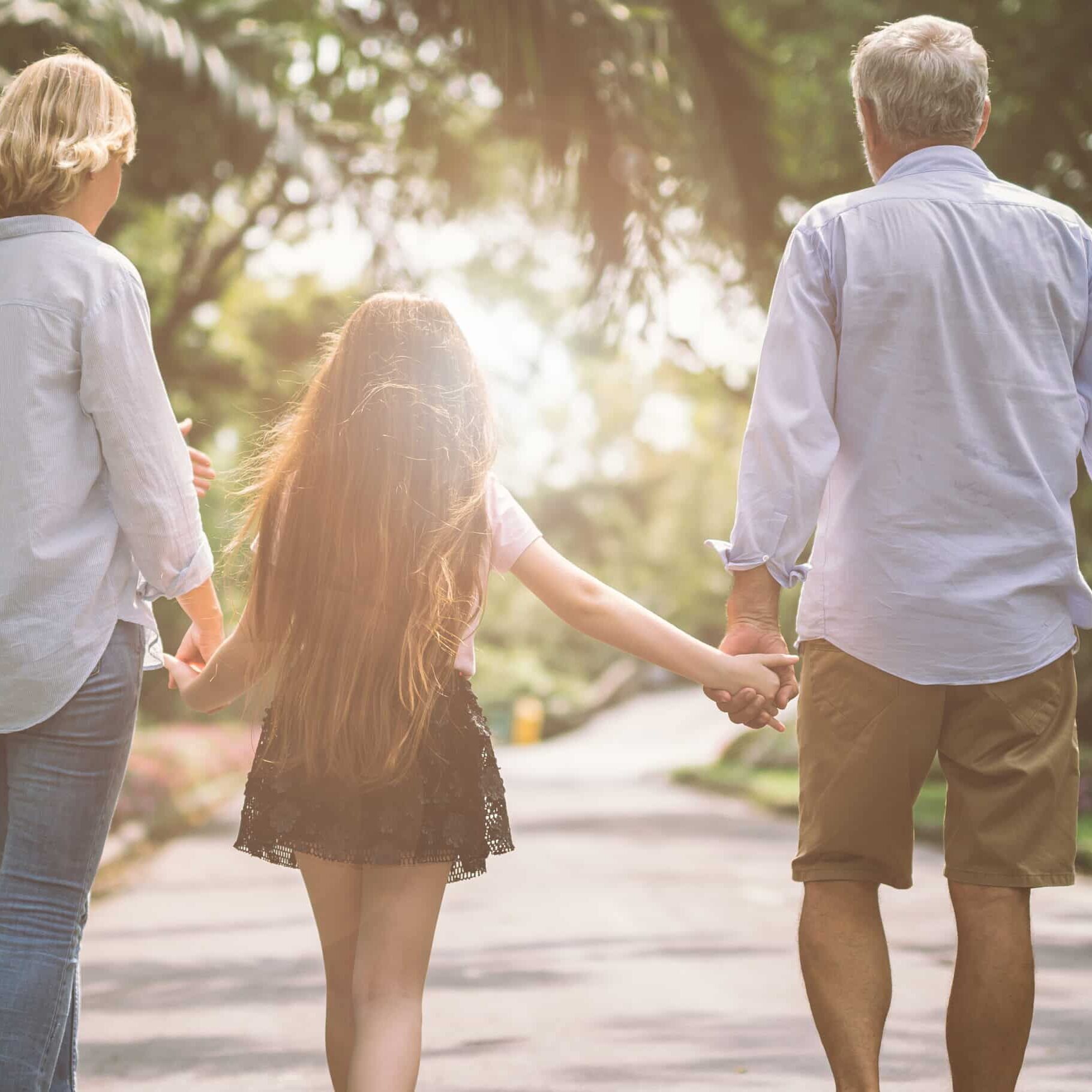 Happy family mother father and daughter walk on nature on sunset hold hand